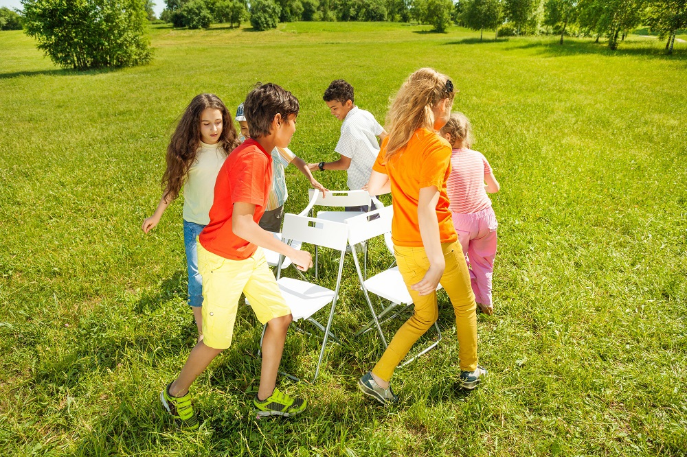 A group of children playing musical chairs in a grassy field